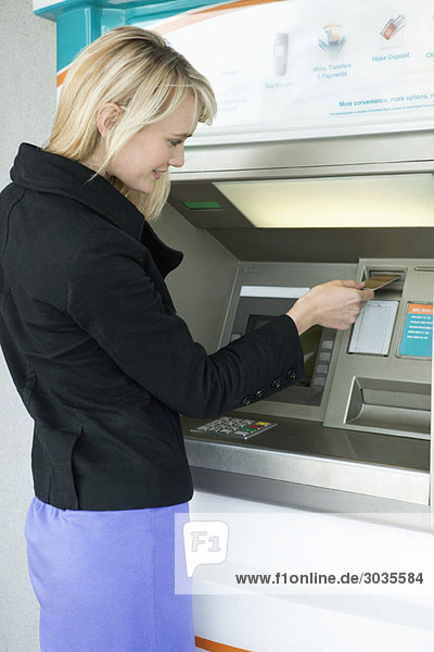 Frau  die eine Kreditkarte in Geldautomat einführt