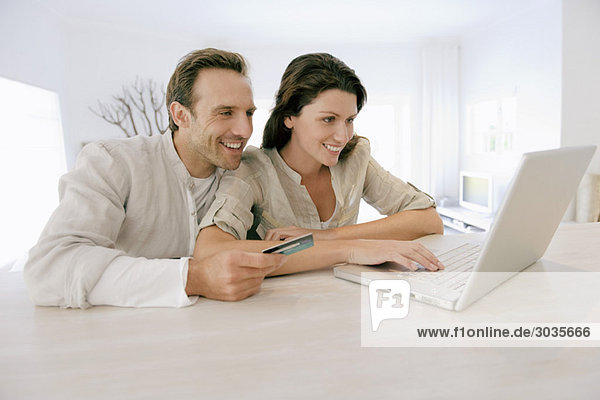 Couple holding a credit card and working on a laptop