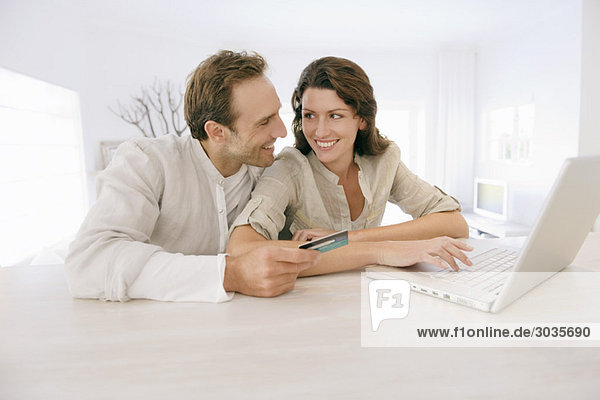 Couple holding a credit card and working on a laptop