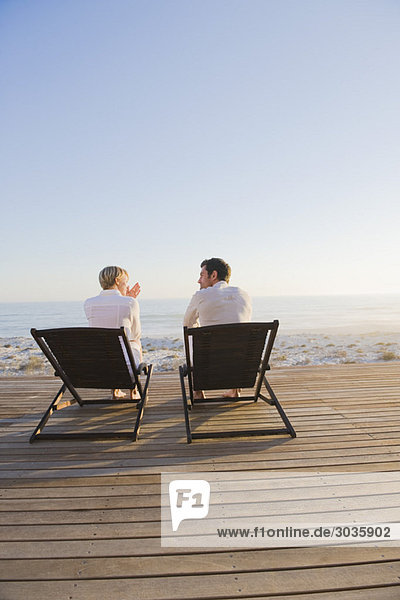 Paar auf Liegestühlen am Strand sitzend
