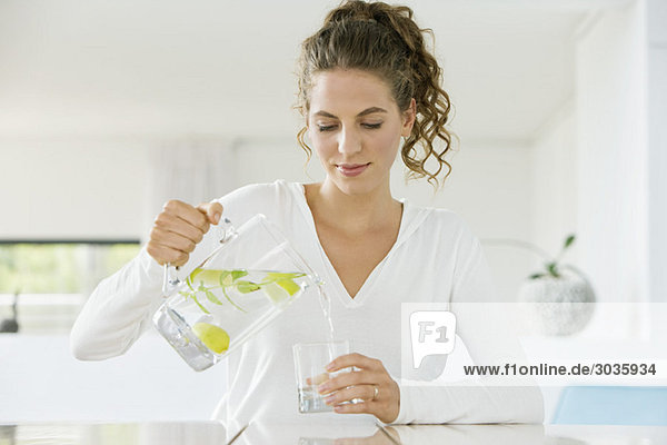Frau gießt Limonade in ein Glas aus einer Kanne