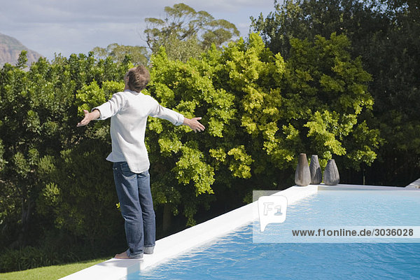 Man standing at the poolside with his arms outstretched