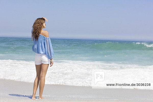Frau am Strand stehend und mit Blick auf die Aussicht