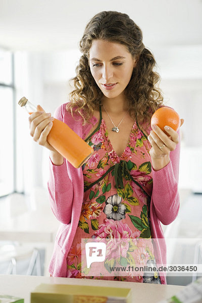 Woman holding orange juice with an orange in the kitchen