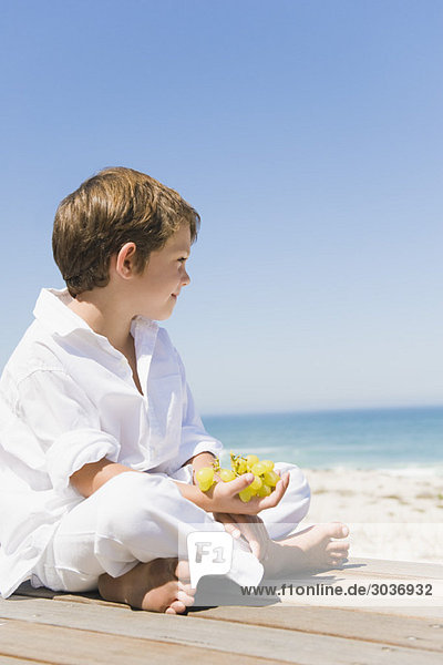 Boy sitting on a boardwalk and holding grapes