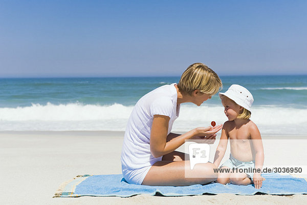 Woman applying suntan lotion on her daughter on the beach