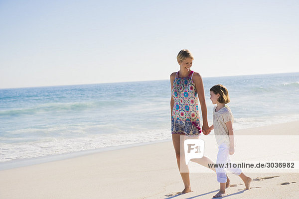 Frau,  die mit ihrer Tochter am Strand spazieren geht.
