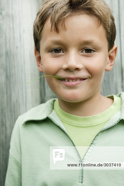 Ein Junge hält einen Grashalm im Mund und lächelt.