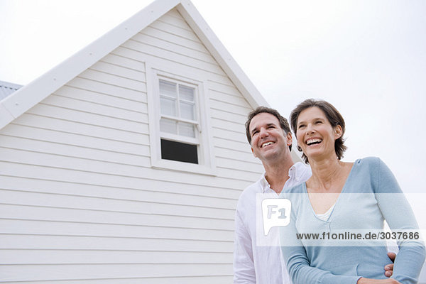 Paar lächelnd mit einem Haus im Hintergrund