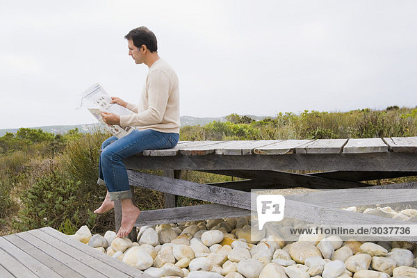 Mann  der auf einer Promenade sitzt und eine Zeitung liest.