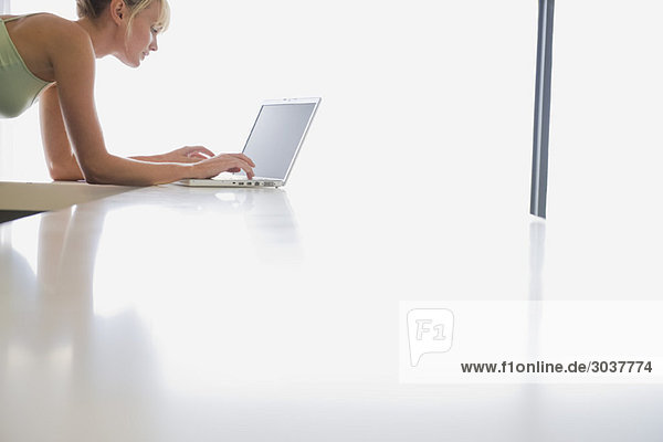 Frau stützt sich auf eine Theke und arbeitet an einem Laptop