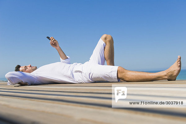 Mann auf einer Promenade liegend und SMS auf dem Handy