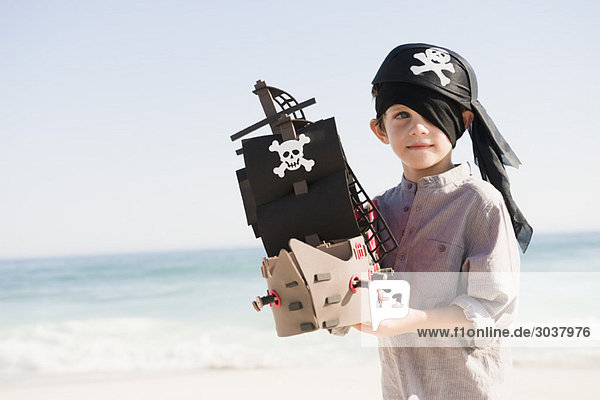 Junge in Piratenkostüm spielt mit einem Spielzeugboot