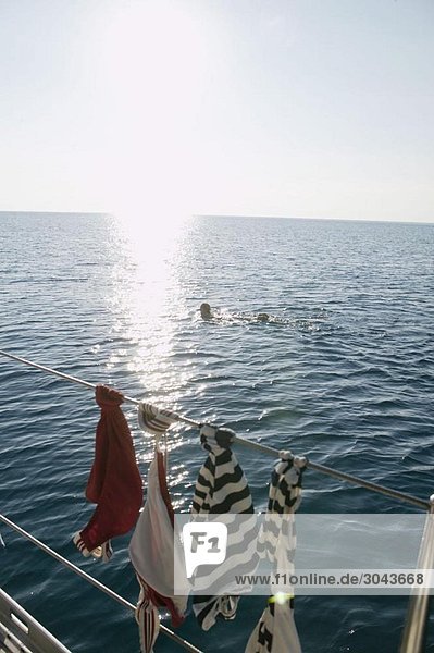Frau schwimmt  während die Kleidung auf dem Boot trocknet.