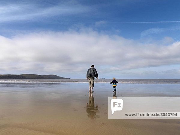 man and child walking towards sea