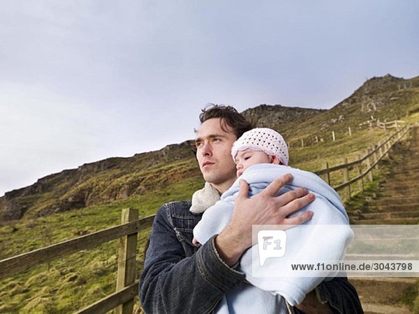 man on hill path holding baby
