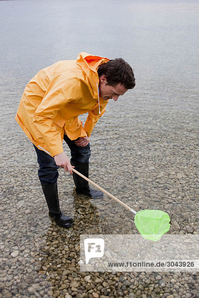 Mann im Regenmantel fischen mit Spielzeugnetz