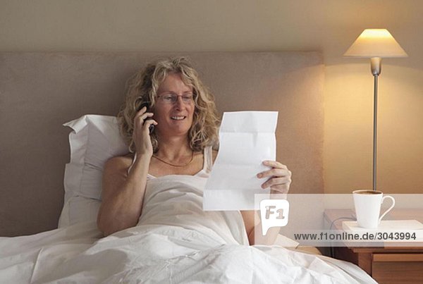 Reife Frau am Telefon im Bett