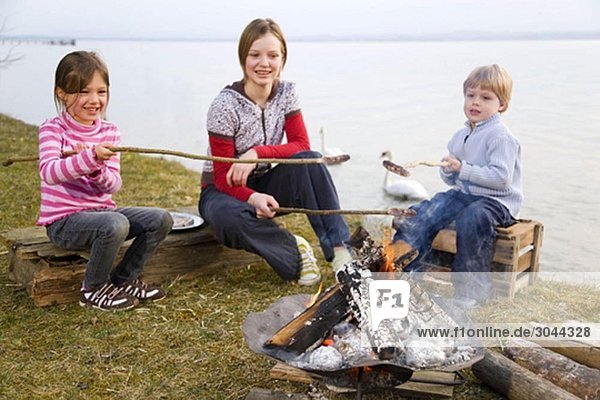 two girls and boy roasting sausages