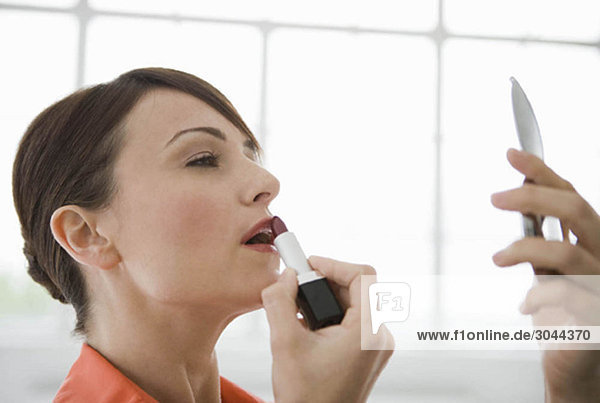Woman applying lipstick in a mirror.