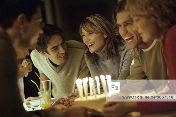 Freunde lachen  lächeln sich an  versammeln sich um den Geburtstagskuchen.