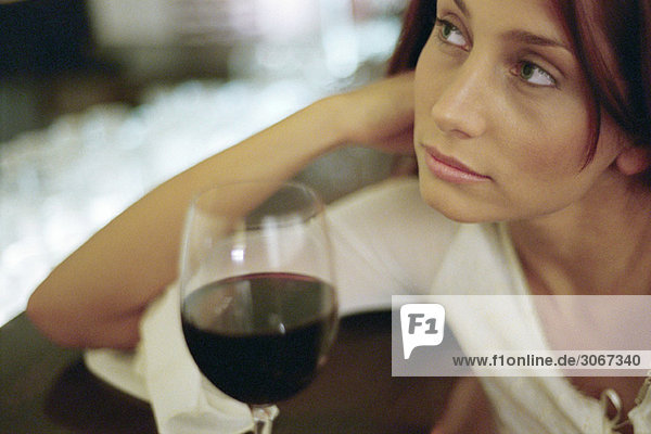 Junge Frau mit einem Glas Wein  an den Ellenbogen gelehnt  wegschauend