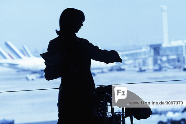 Silhouette einer Reisenden mit Blick auf die Uhr am Flughafen