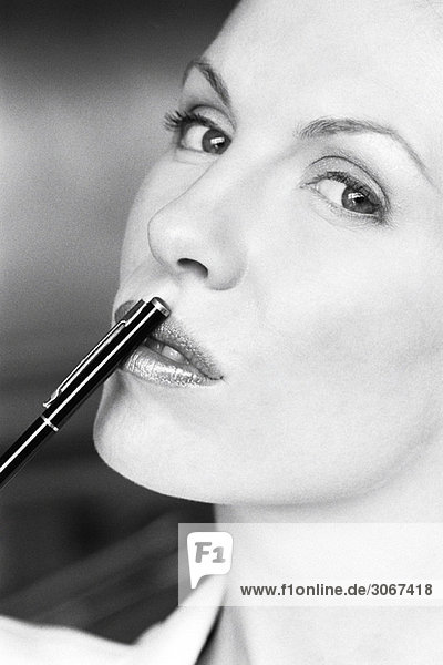 Frau berührt die Lippen mit dem Stift  blickt zur Seite in die Kamera
