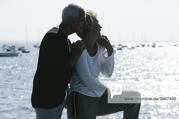 Mature couple standing together on pier  looking at view  backlit