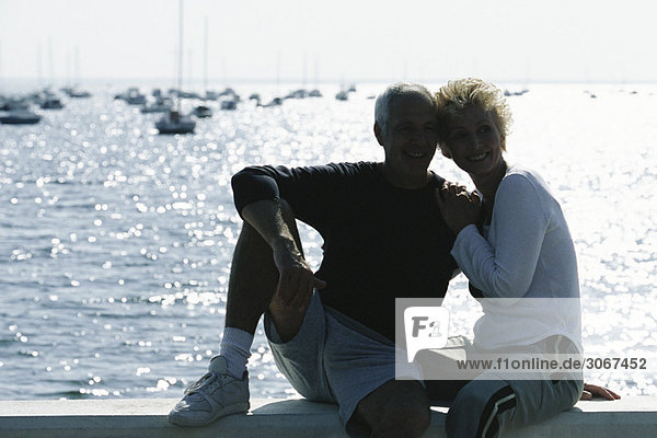 Mature couple sitting together on pier  backlit