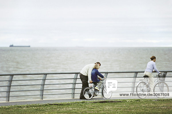 Vater hilft dem Sohn beim Fahrradfahren im Seepark  Mutter fährt voraus