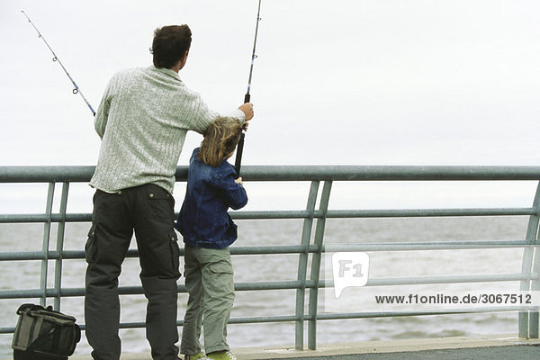 Vater und Sohn fischen vom Pier aus  Vater hilft dem Sohn mit seiner Angelrute.