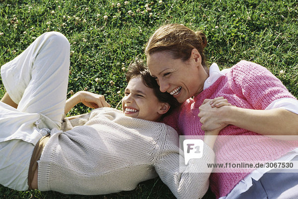 Mutter und Tochter im Gras liegend  lachend  Händchen haltend