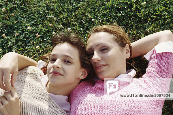 Mutter und Tochter liegen zusammen auf Gras und lächeln in die Kamera.