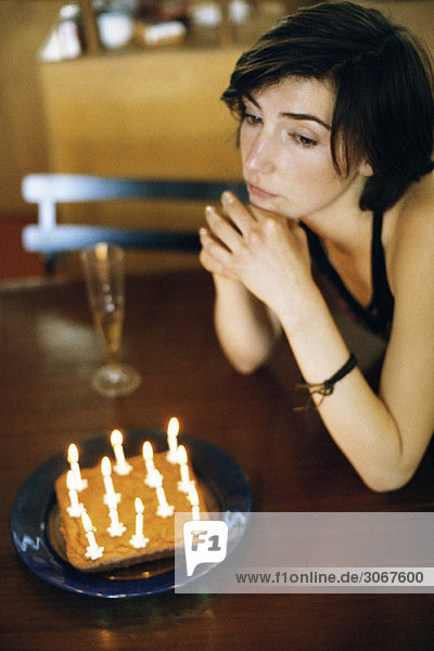 Woman at table with birthday cake looking away wistfully