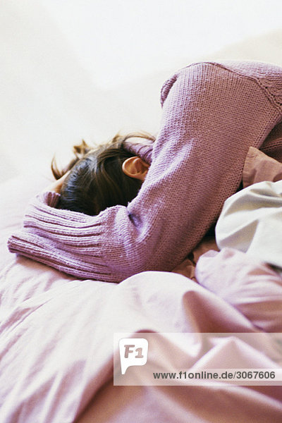 Woman lying on bed covering face with arm