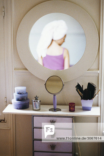 Reflection of woman with head wrapped in towel in mirror hanging above woman's dressing table