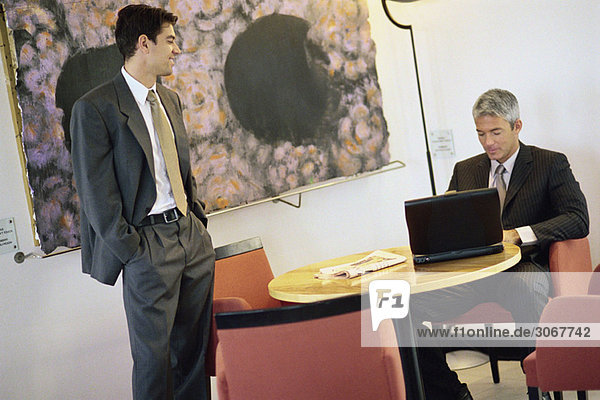 Businessmen chatting in break room  one using laptop computer
