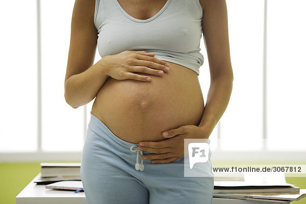 Schwangere Frau mit Händen auf nacktem Bauch  Mittelteil