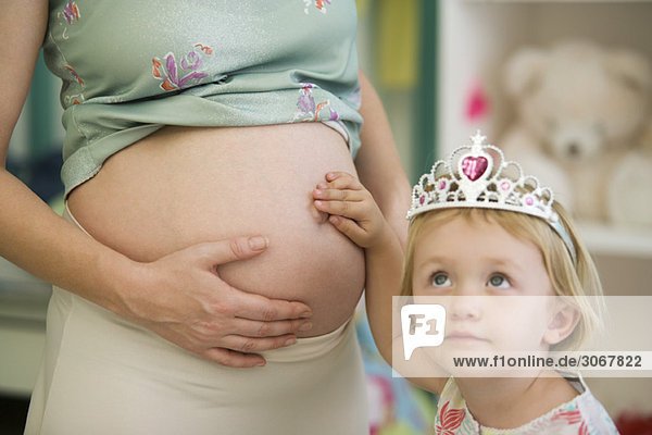 Kleines Mädchen berührt Mutters schwangeren Bauch