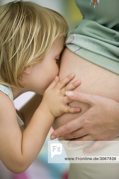Kleines Mädchen küsst den schwangeren Bauch der Mutter.