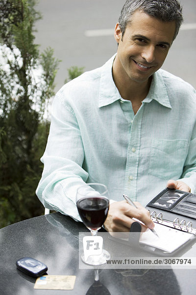 Man sitting at outdoor cafe table with glass of wine  writing in agenda