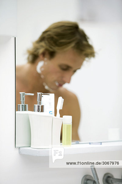 Mann mit Rasiercreme im Gesicht im Badezimmerspiegel reflektiert