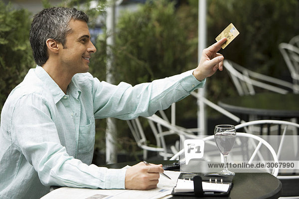 Mann sitzt in einem Café im Freien und hält eine Kreditkarte aus  um zu bezahlen.