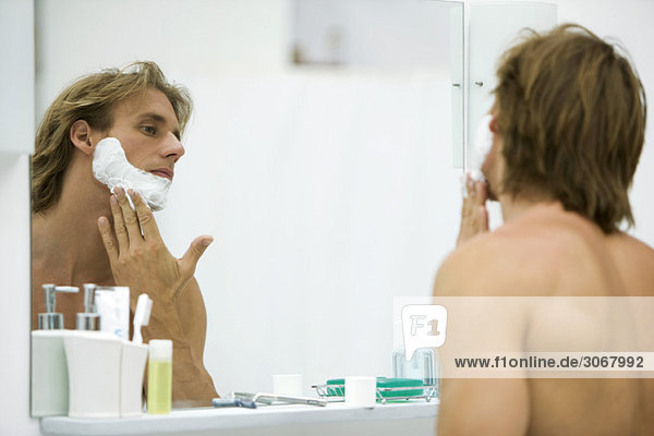 Mann beim Auftragen von Rasiercreme im Badezimmerspiegel