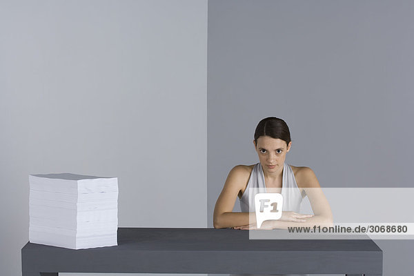 Frau sitzt am Tisch neben großem Papierstapel  Arme gefaltet  schaut in die Kamera