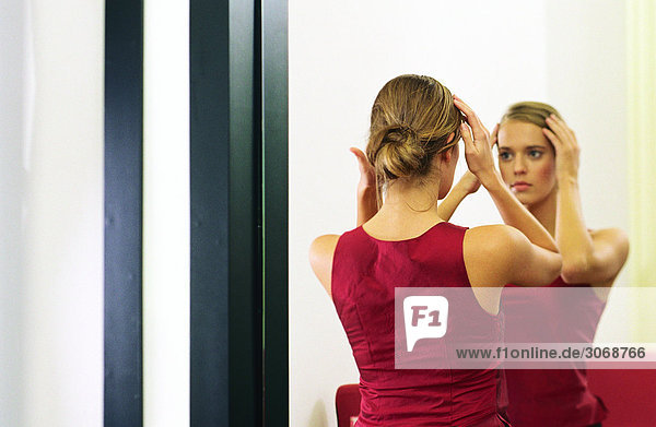 Frau schaut in den Spiegel und berührt das Haar.