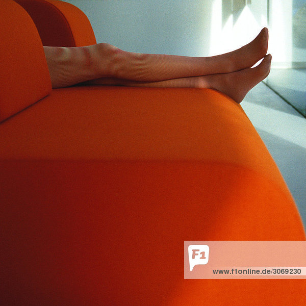 Frauenbeine auf orangefarbenem Sofa