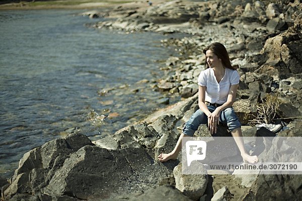 Eine junge Frau sitzend auf Klippen am Meer Ingaro Schweden