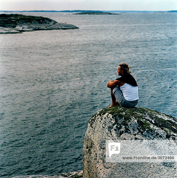 Eine Frau sitzend auf einem Felsen am Meer Schweden